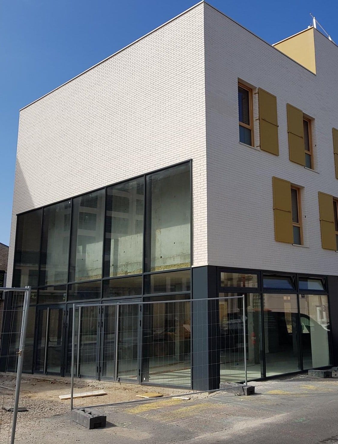 Bâtiment neuf en brique claire, mur-rideau aluminium double hauteur sur une façade jusqu'à l'angle, ensembles vitrés au rez-de-chaussée