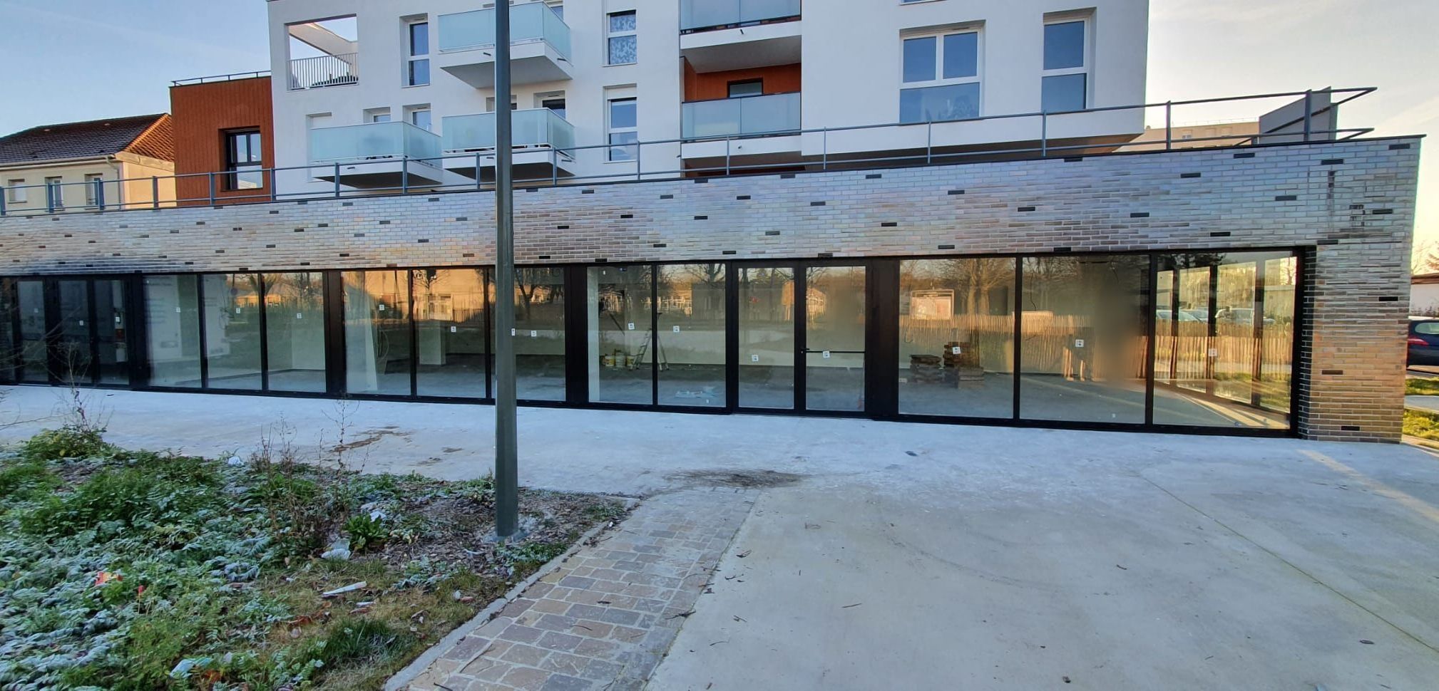 Rez-de-chaussée d'immeuble vitré par un ensemble de portes et de fenêtres aluminium foncées, sous une façade en brique
