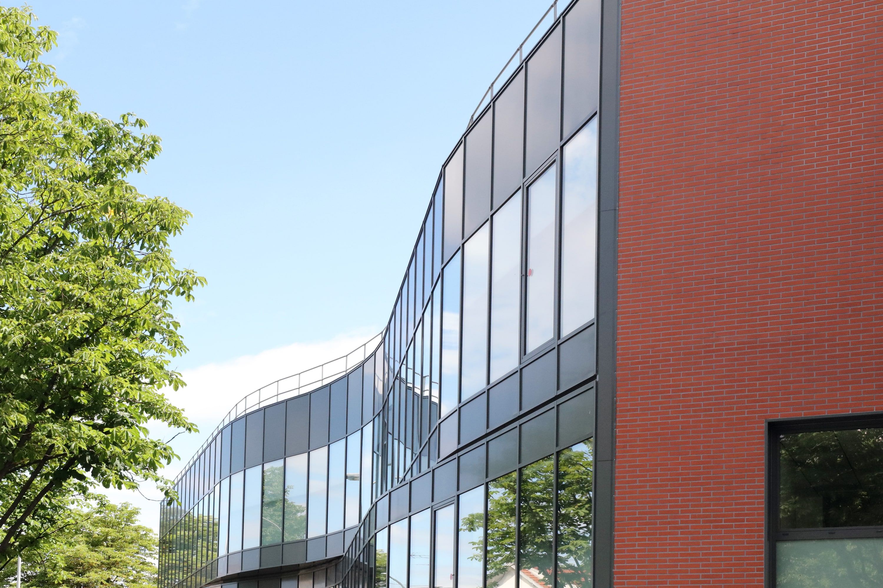 Façade vitrée de la crèche de Créteil prolongée par un pignon en brique rouge, vue depuis la rue