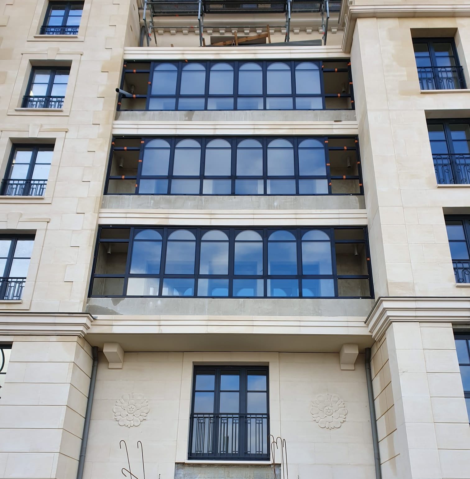 Façade d'immeuble en pierre claire, ensembles de fenêtres aluminium foncées à impostes cintrées superposés sur plusieurs étages