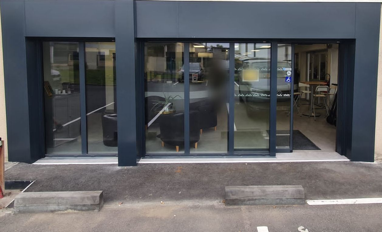 Entrée d'un local professionnel : deux ensembles vitrés aluminium dont une porte automatique, dans un encadrement gris anthracite