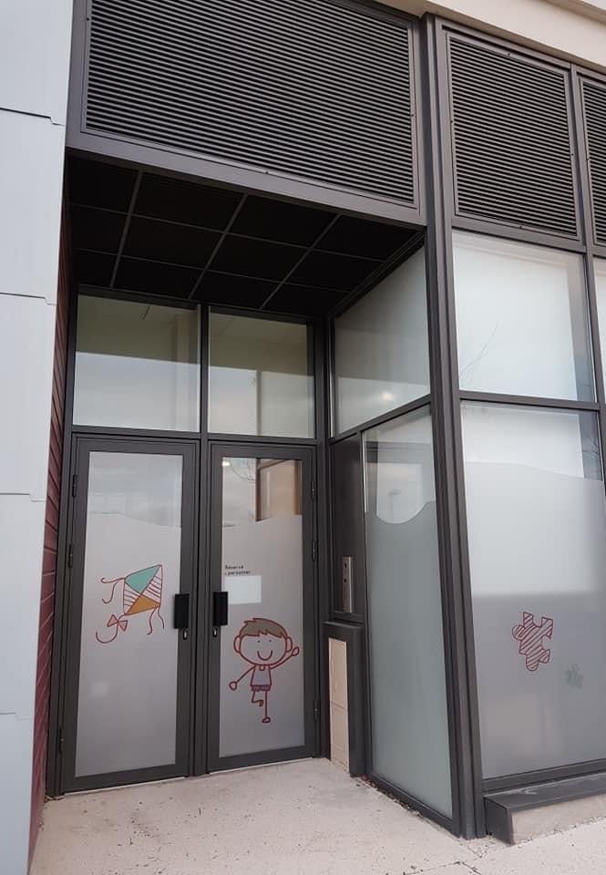 Double porte vitrée aluminium à l'entrée d'une crèche, vitrages décorés de dessins d'enfants