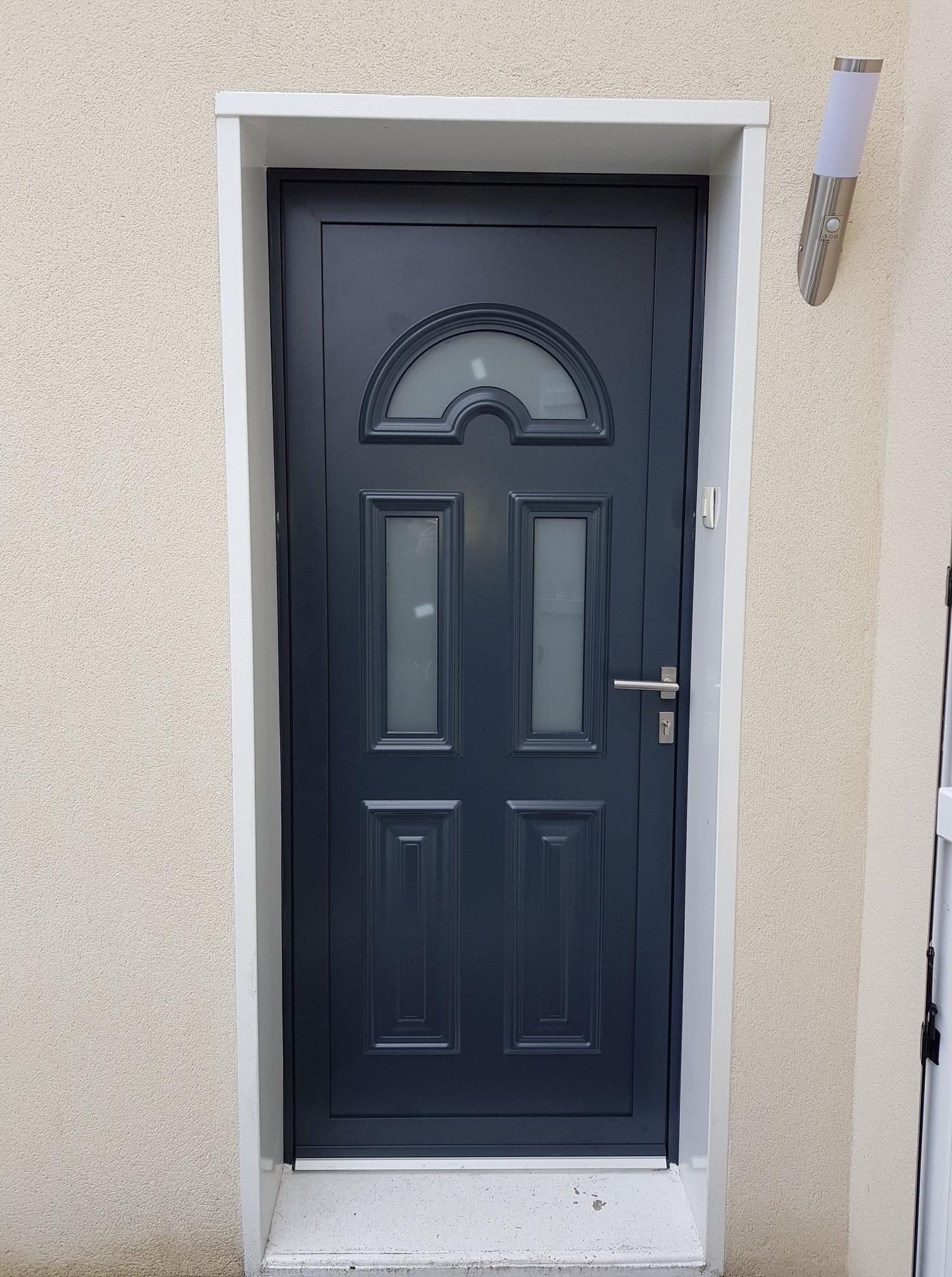 Porte d'entrée aluminium gris anthracite à panneaux moulurés et vitrages décoratifs, posée dans un mur enduit clair