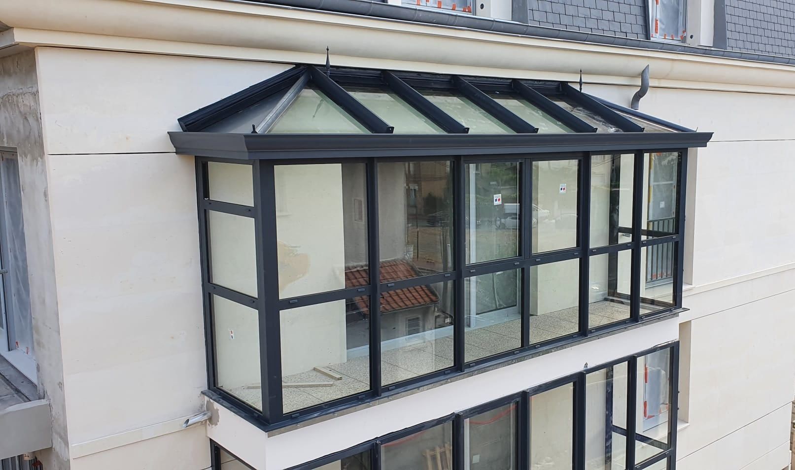 Véranda aluminium gris anthracite à toiture vitrée, fermant la terrasse d'étage d'un immeuble